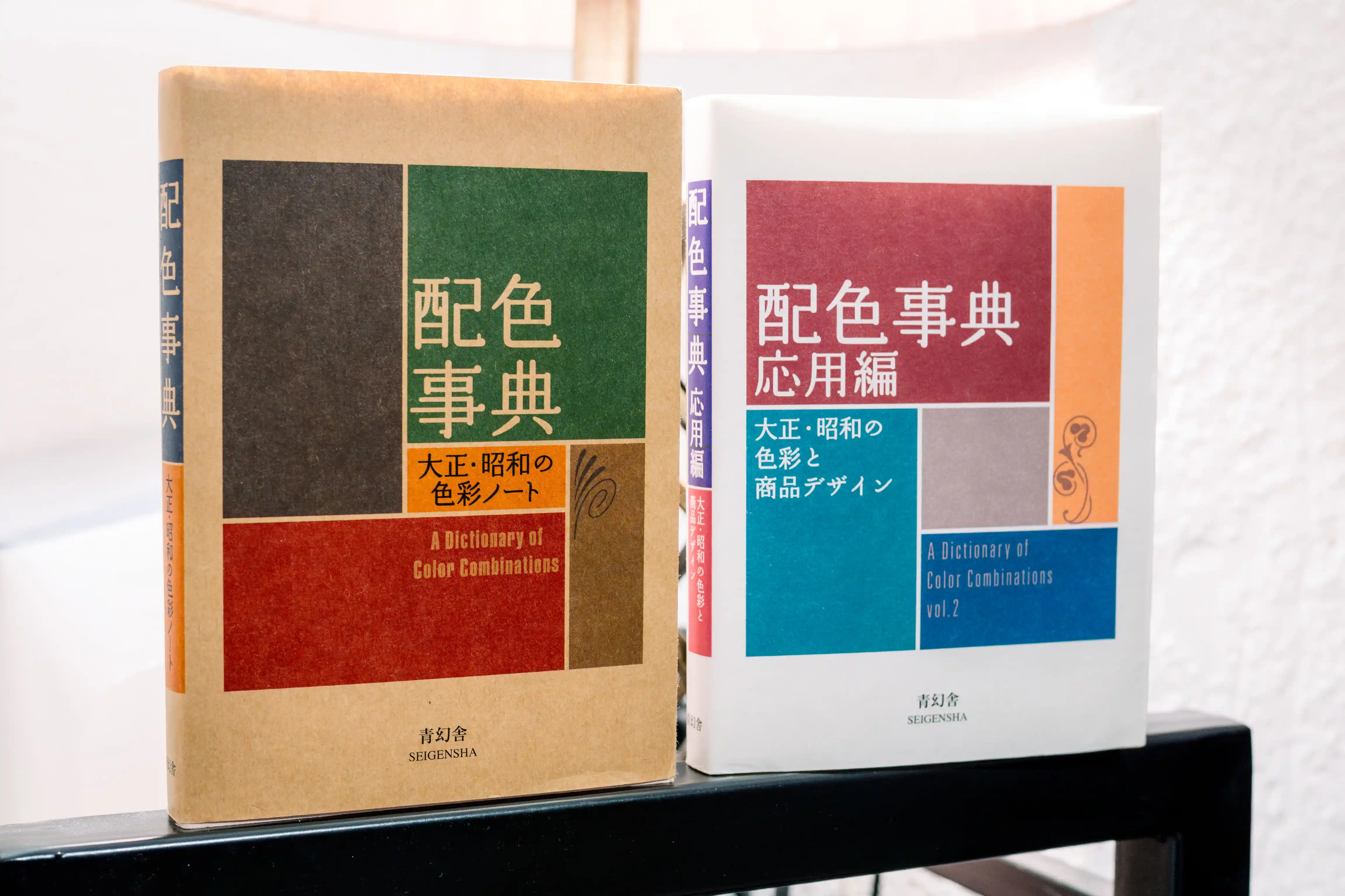 Los dos volúmenes de los catálogos de combinaciones de color de Sanzō Wada publicados por Seigensha. Al fondo, una lámpara que ilumina la escena